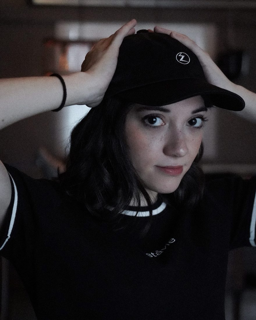 Lexi Oliver in a black cap, hands on her head, smiling slightly