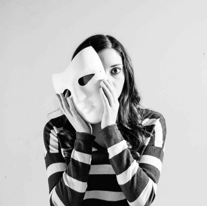 Black and white photo of Lexi holding a white mask over half her face